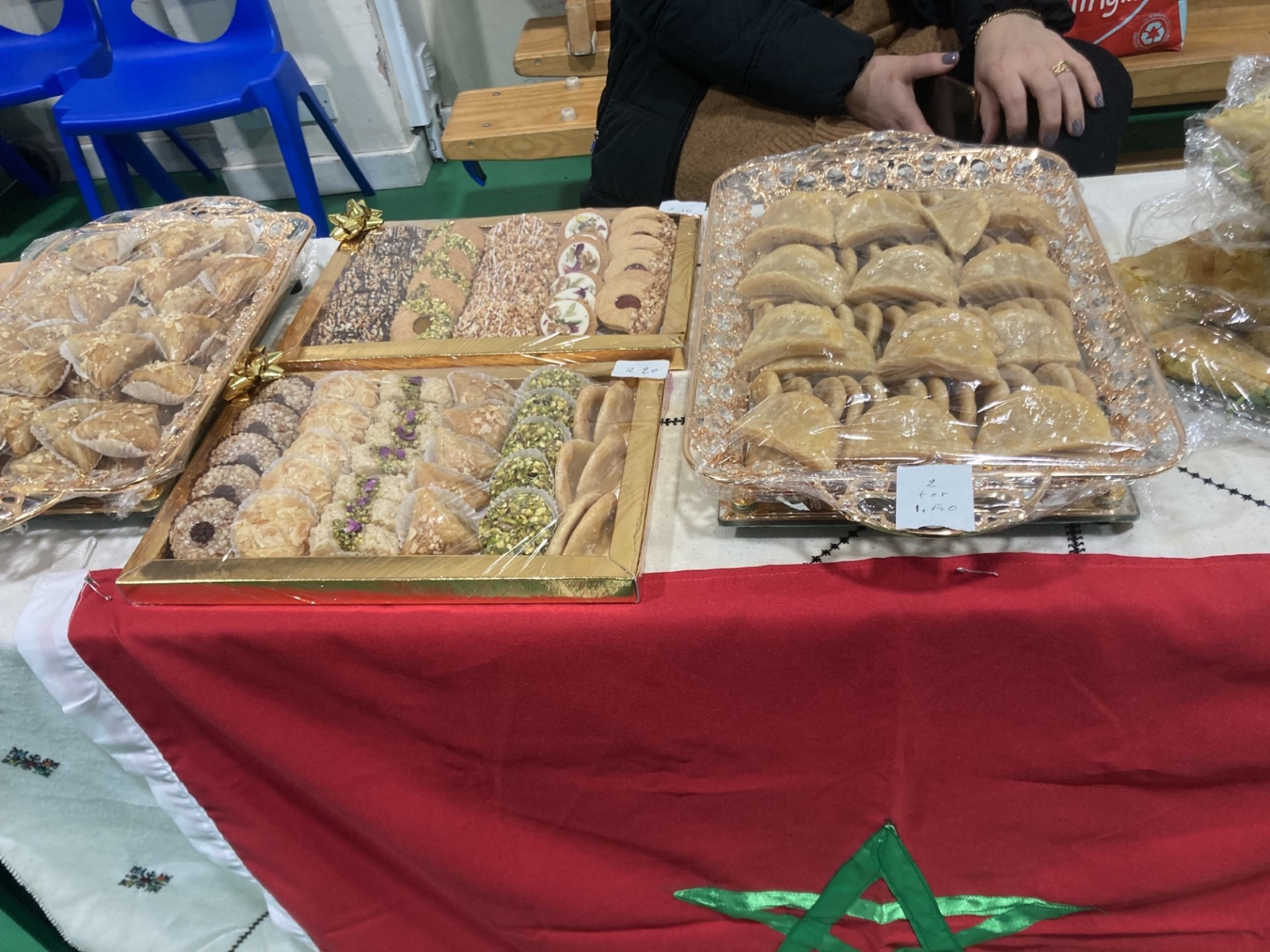 Trays of Moroccan baklava and pastries on a stand draped with the Moroccan flag